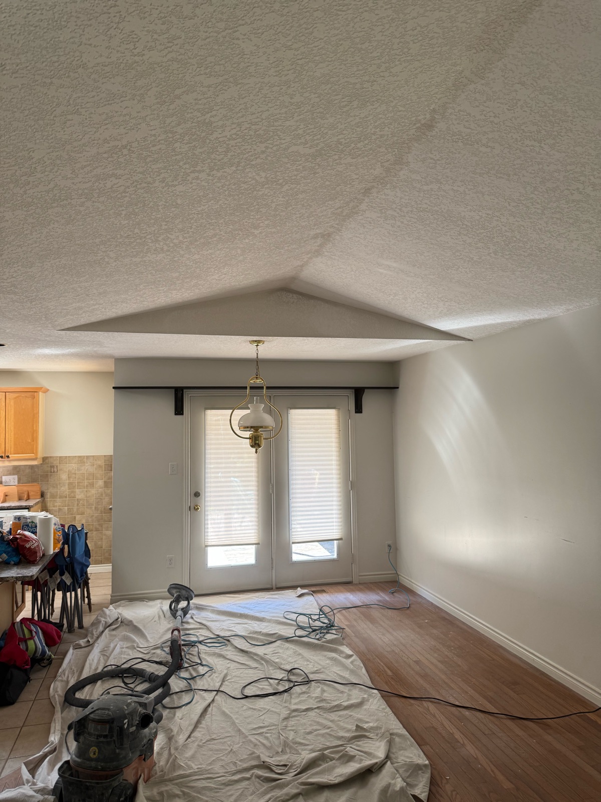 Orange peel textured vaulted ceiling before removal, with a drop sheet on the floor and a sander and vacuum set up