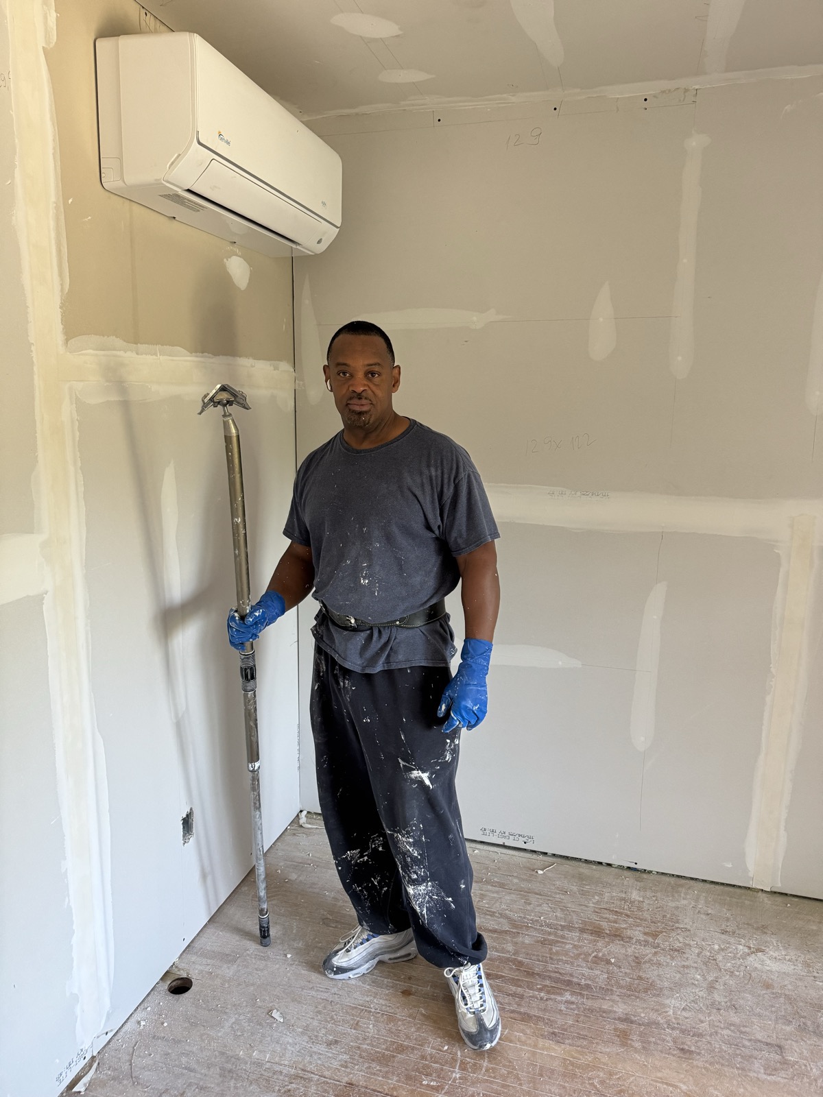 Gary standing in a finished, taped room holding a pole sander
