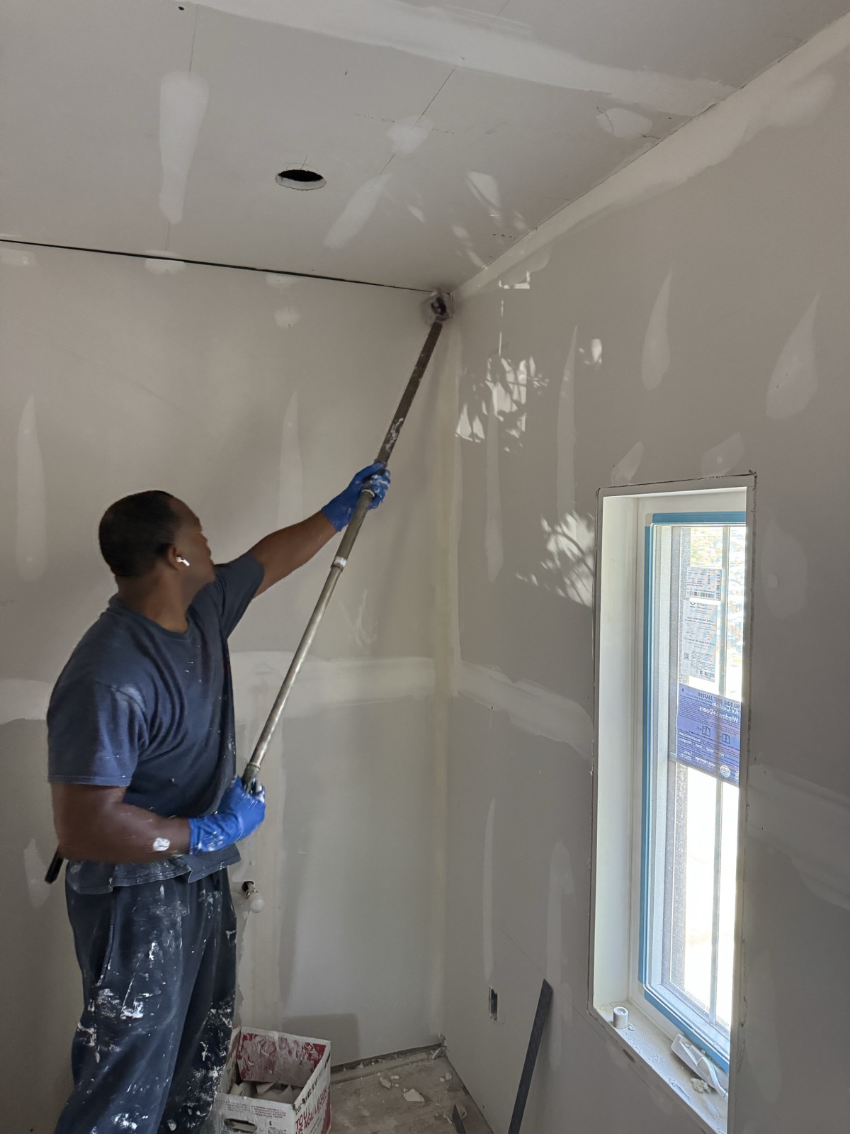Gary pole-sanding a wall beside a window
